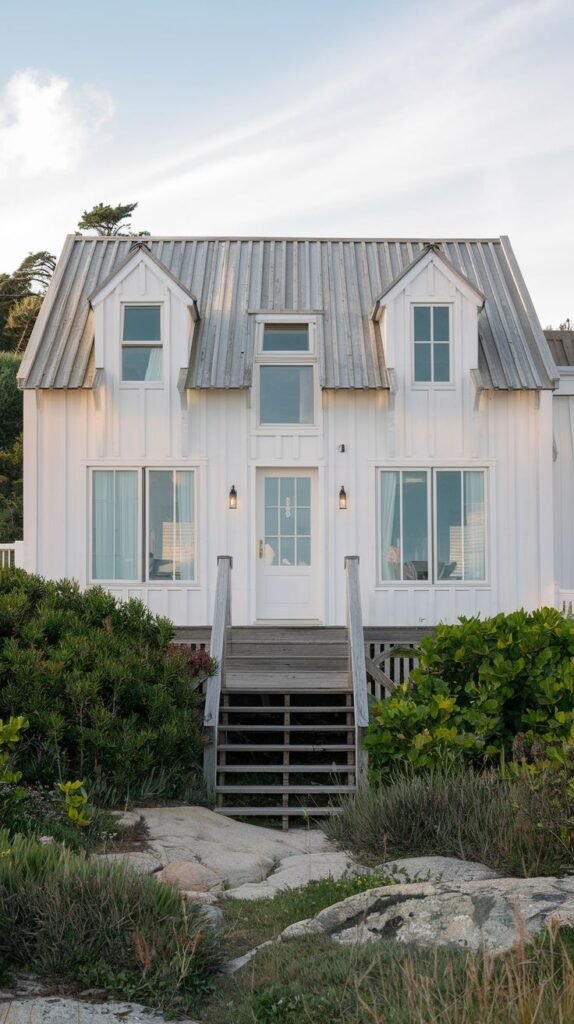 Beautiful coastal cottage with white board and batten siding and a metal roof, viewed from wooden stairs.