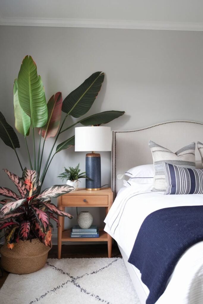 A large Bird of Paradise plant in a woven basket is placed next to a nightstand and bed, with a smaller plant on the nightstand.