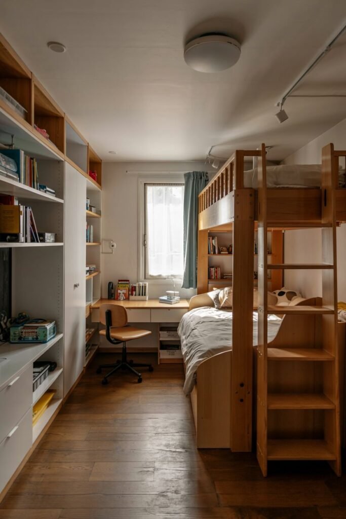 Chic kids' bedroom with a wooden bunk bed, a desk area beneath the top bunk, and tall built-in shelves along the wall.