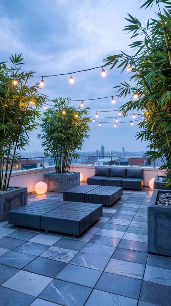 A modern rooftop lounge area at dusk, featuring plush modular seating and large potted bamboo, illuminated by cozy string lights, with a city view in the background.