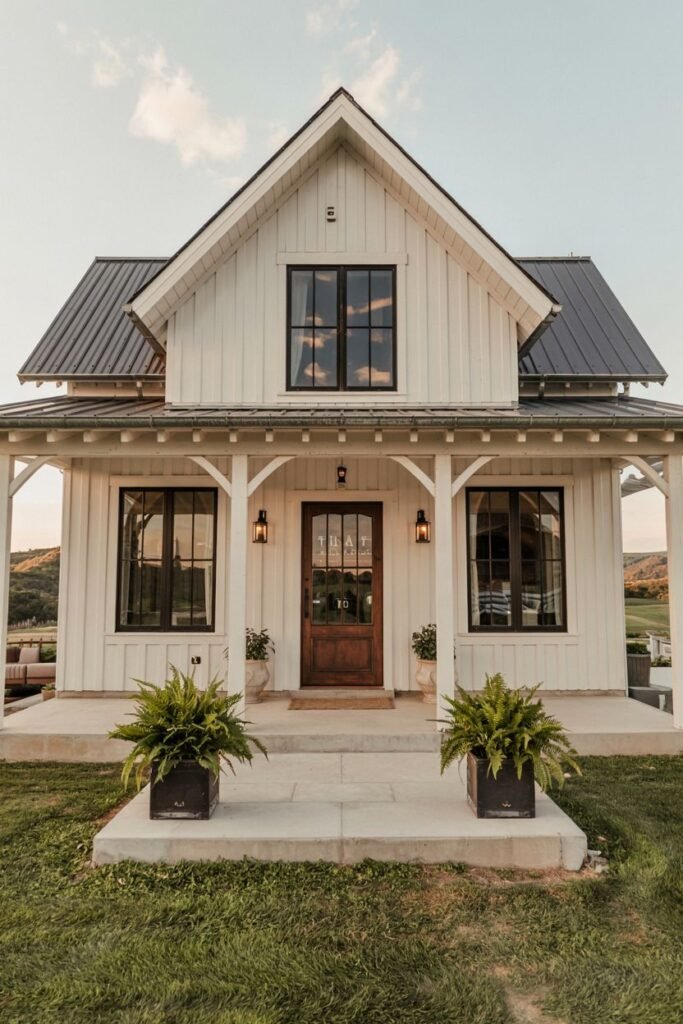 A white two-story modern farmhouse with board-and-batten siding, a dark metal roof, dark windows, and a small front porch with a natural wood door.