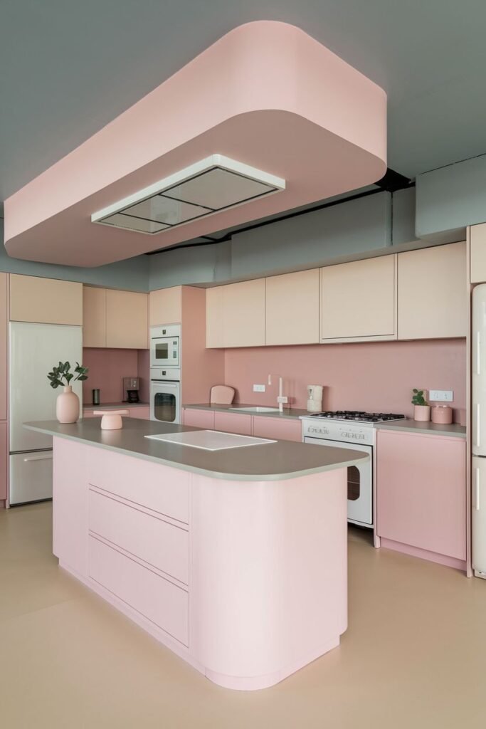 Modern pastel kitchen in shades of light pink and beige. It includes a pink kitchen island with rounded edges and a unique pink overhead structure for the hood.