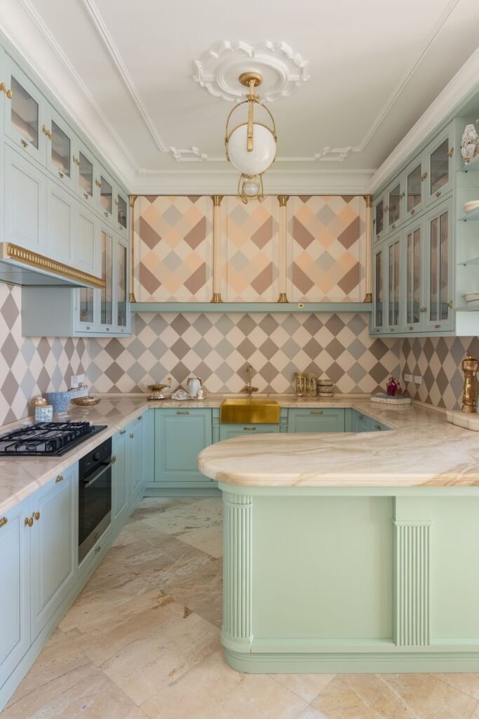 Elegant pastel kitchen with light blue cabinets and a light green kitchen island, both with decorative trim. A gold sink is integrated into the countertop, and the backsplash features a diamond pattern in pastel colors.