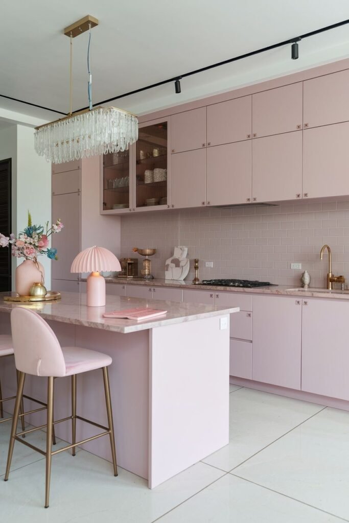 Contemporary pastel kitchen featuring light pink cabinets and a pink kitchen island with a marble countertop. The backsplash is a light pink tile.