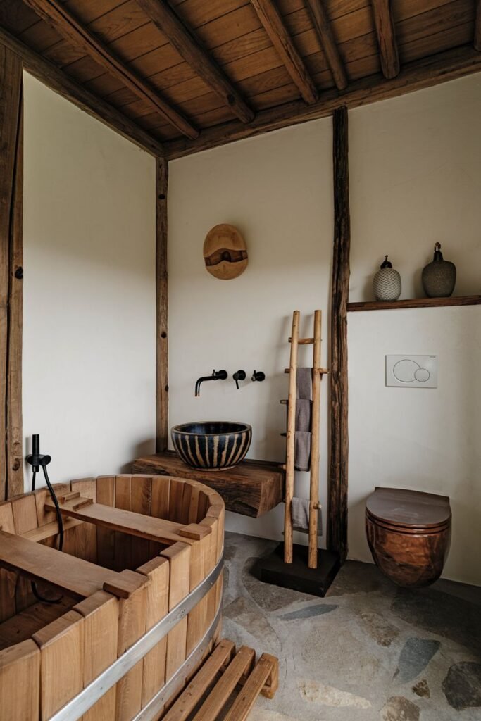 A bathroom with a light wooden barrel-shaped bathtub with metal bands, a striped ceramic sink on a wooden counter, a wooden ladder used as a towel rack, and a modern toilet.