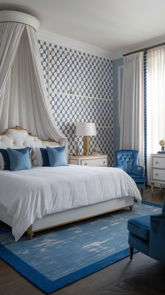 A beautiful and dreamy bedroom with a white canopy bed, blue pillows, and a blue and white patterned accent wall, featuring a blue tufted armchair and a blue rug with a lighter border.