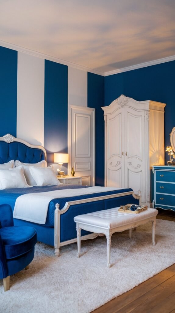 A beautiful and dreamy modern bedroom with a dramatic blue and white striped accent wall, featuring a blue upholstered bed, a white tufted bench, a white wardrobe, and a soft white rug.