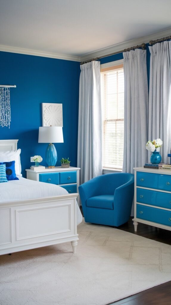 A beautiful and dreamy bedroom showcasing a vibrant blue accent wall, a white bed, a blue armchair, white nightstands with blue accents, and white curtains framing a window.