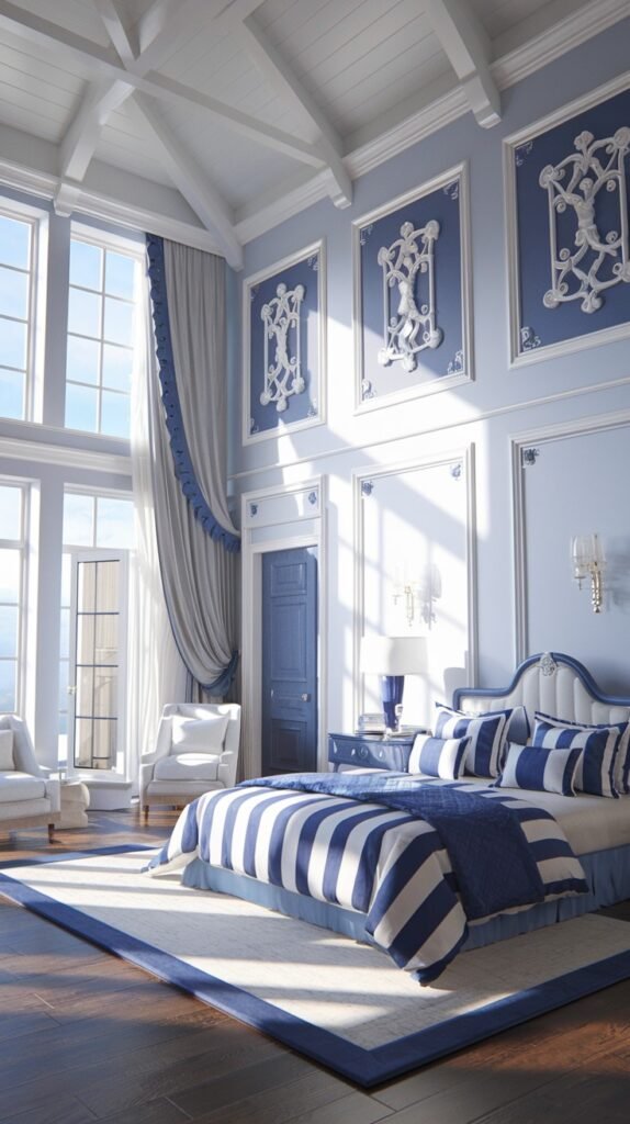 A beautiful and dreamy grand bedroom with very tall windows, light blue walls with decorative white molding and art, and a white bed with bold blue and white striped bedding.
