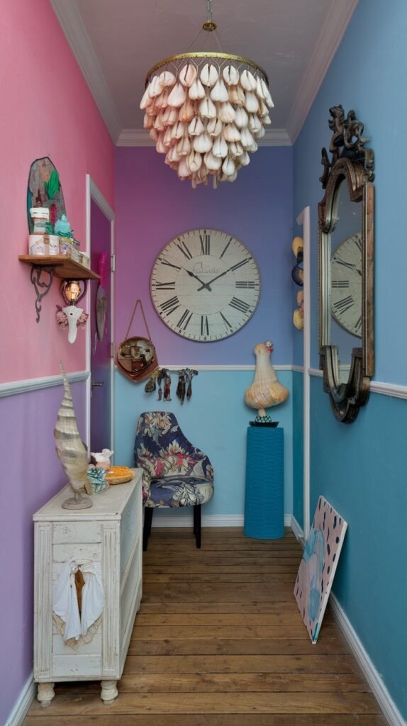 A colorful and quirky hallway showcasing a distinct blend of pastel pink, purple, and blue wall sections. The space features an antique-style white cabinet, a shell-encrusted chandelier, a large round clock with Roman numerals, and a unique floral-patterned chair, alongside various whimsical decorative objects and a large ornate mirror.