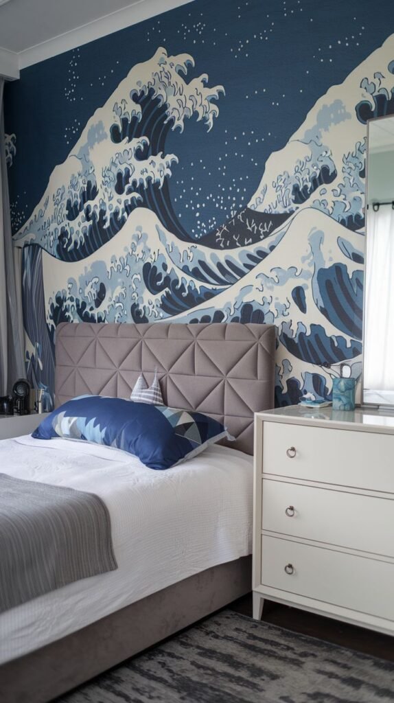 A bedroom wall displaying a dramatic ocean wave mural in various shades of blue and white, reminiscent of classic Japanese art. A grey upholstered bed and a white dresser are visible.