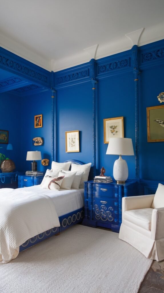 A richly detailed and cozy bedroom with deep blue walls featuring intricate paneling and molding. The room includes a white bed with a blue upholstered base, matching blue nightstands with white lamps, and a light-colored rug, contributing to a luxurious and cozy setting.