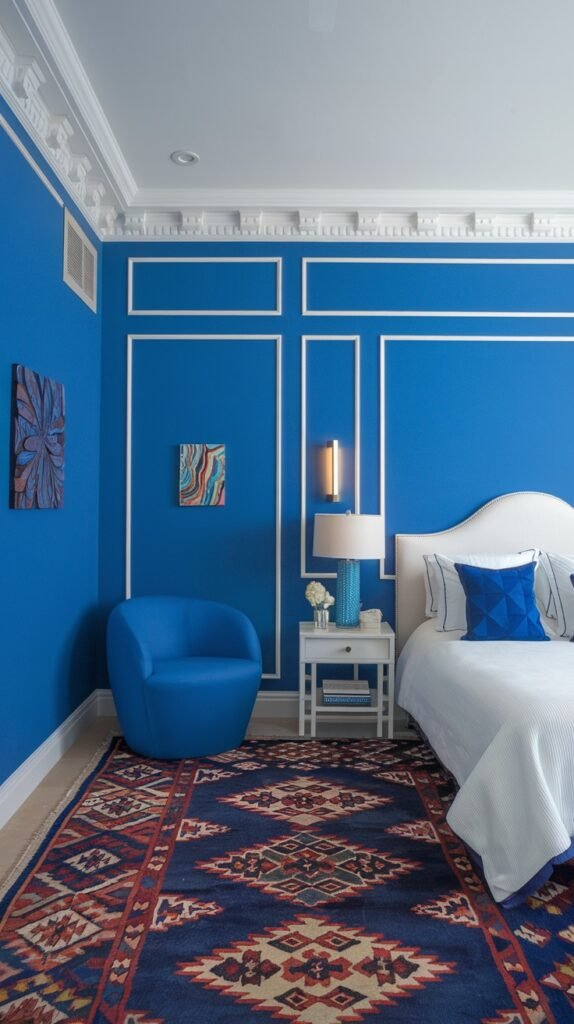 A stylish and cozy bedroom with deep blue paneled walls accented by crisp white trim. The room contains a white bed, a round blue accent chair, and a richly patterned rug with blue and red tones, creating a distinct and cozy design.