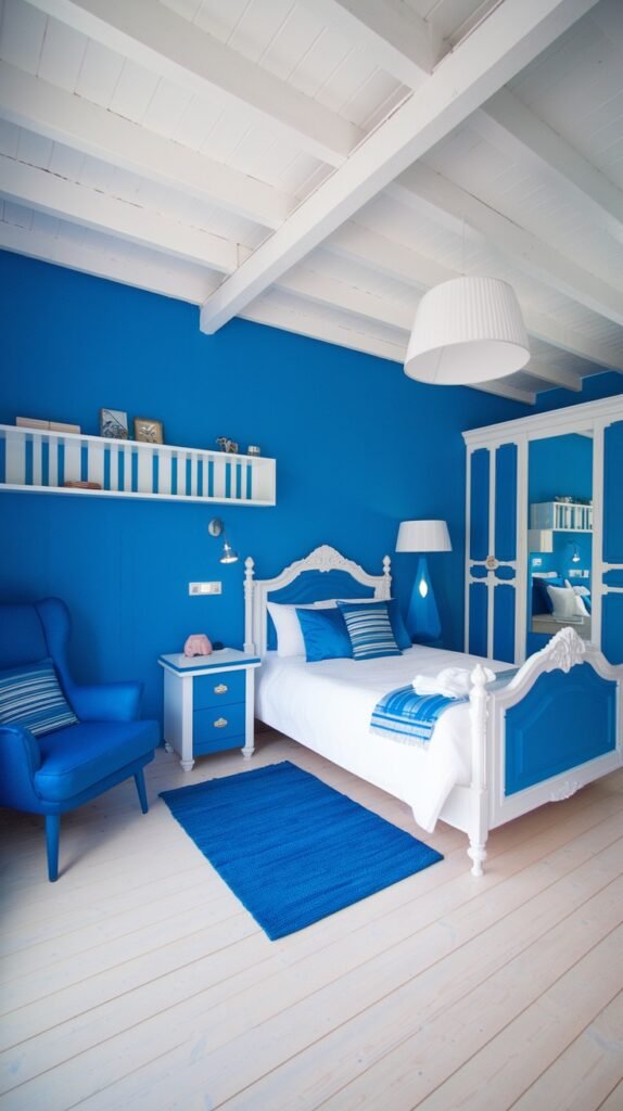 A cozy bedroom with vivid blue walls and a white exposed beam ceiling. The room features a white traditional bed frame with a blue upholstered base, white furniture including a wardrobe and nightstand, and a blue rug, creating a fresh and cozy ambiance.