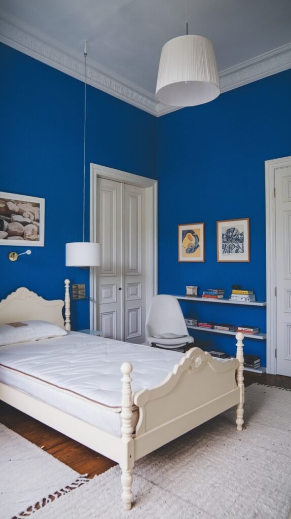 This cozy bedroom has vibrant blue walls and features a classic white bed frame with a white mattress. A textured white rug covers the floor, and a white pendant lamp hangs from the ceiling, adding to the room's calm and cozy ambiance.