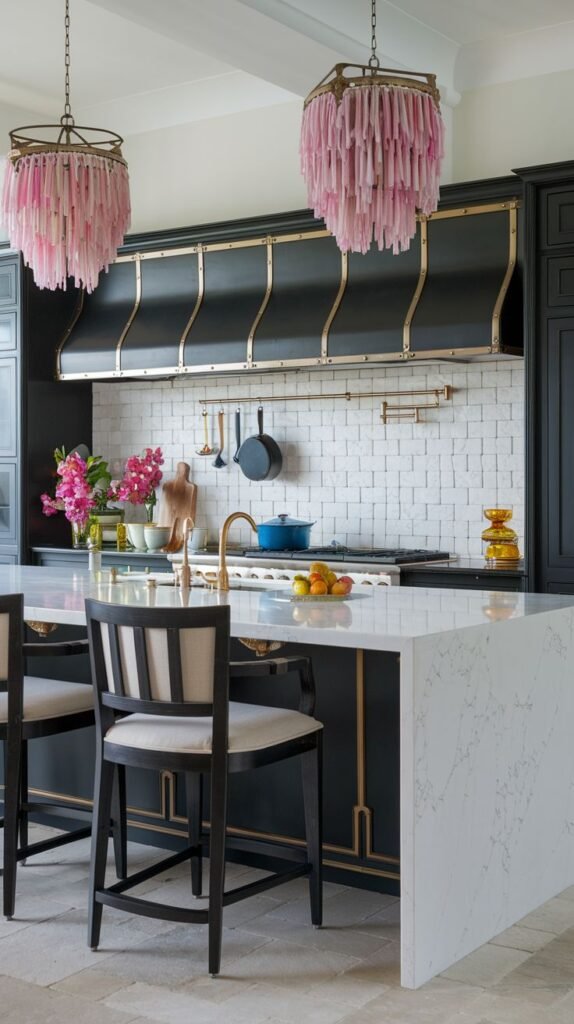 A dynamic Black and White kitchen showcases dark cabinetry with brass accents and a white subway tile backsplash. Two prominent pink fringed chandeliers hang above a large white marble island, adding a pop of color to the sleek design.