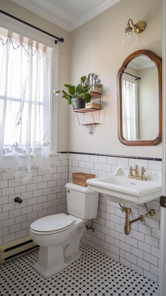 A cozy half bathroom with white subway tiles on the lower walls and a light beige painted upper wall, separated by a black trim. It includes a white toilet and a white wall-mounted sink with gold fixtures. A window with sheer white curtains is on the left, and a black metal wall shelf with a plant is mounted between the window and a wooden-framed mirror.