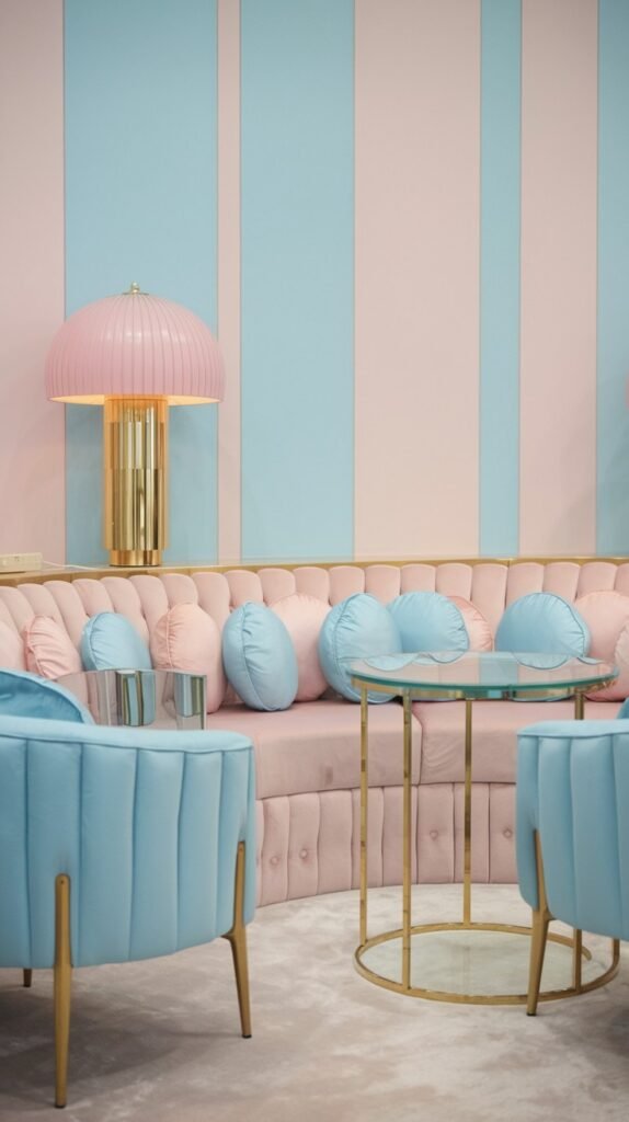 A vibrant and luxury pastel room showcasing vertical stripes in pastel pink and pastel blue, with a pastel pink tufted sofa, pastel blue round cushions, pastel blue armchairs, and a distinctive pastel pink luxury table lamp.