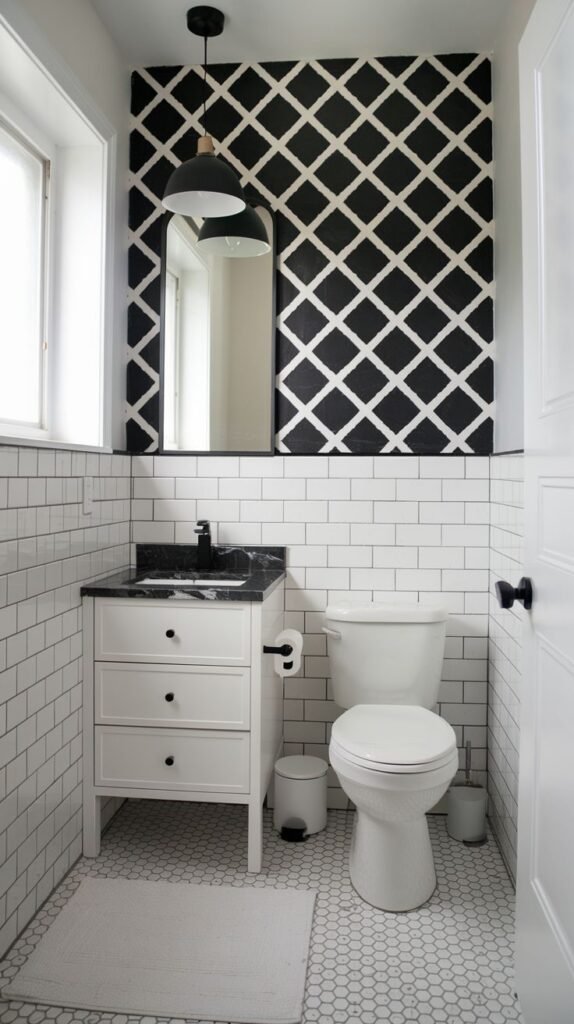 A small, modern powder room distinguished by a bold black and white geometric patterned accent wall above classic white subway tiles. It features a white vanity with a black countertop, a toilet, and a hexagon-tiled floor.