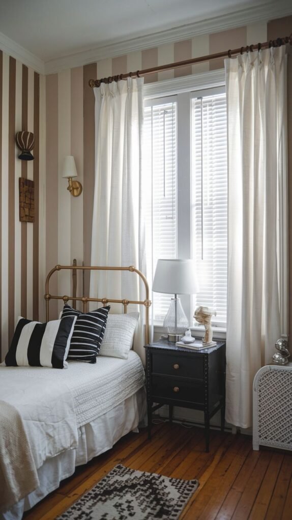 An inviting Apartment One Bedroom with warm striped wallpaper, a brass bed frame, a black nightstand, and black and white striped pillows on the bed.