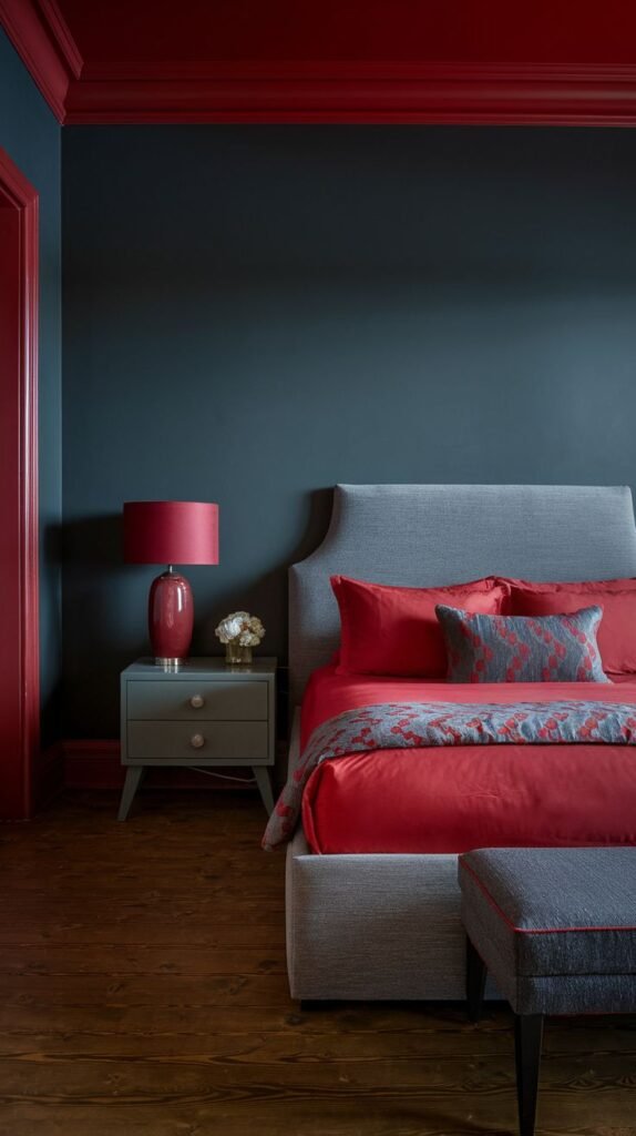 A sophisticated bedroom with bold redecorating choices, featuring deep blue walls contrasted with vibrant red trim and red bedding on a gray upholstered bed.