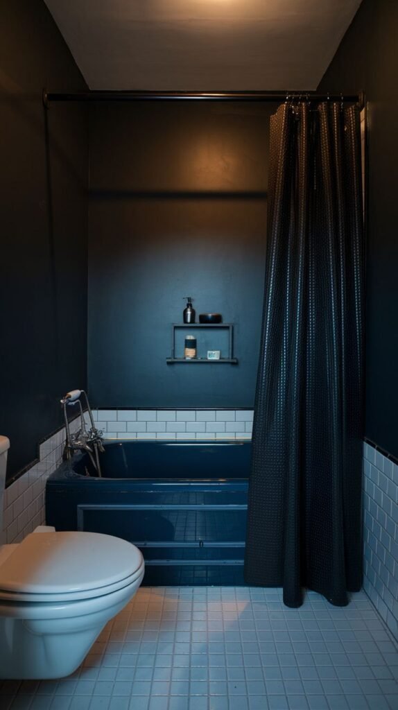 A tiny, moody bathroom with dark blue upper walls, white subway tiles around a dark blue bathtub, and a light-colored tiled floor. A black shower curtain is pulled across the tub.