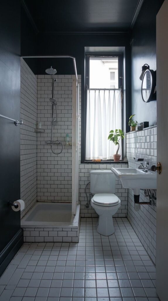 A tiny, moody bathroom primarily featuring white subway tiles on the walls and a white tiled floor. It includes a shower stall, a white toilet, a small white sink, and a window with a white curtain.