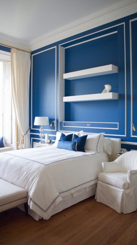 Classic Blue Wall with White Panel Molding and Recessed Shelves Classic blue accent wall defined by white panel molding, featuring a central recessed section containing two thick white floating shelves over a bed.
