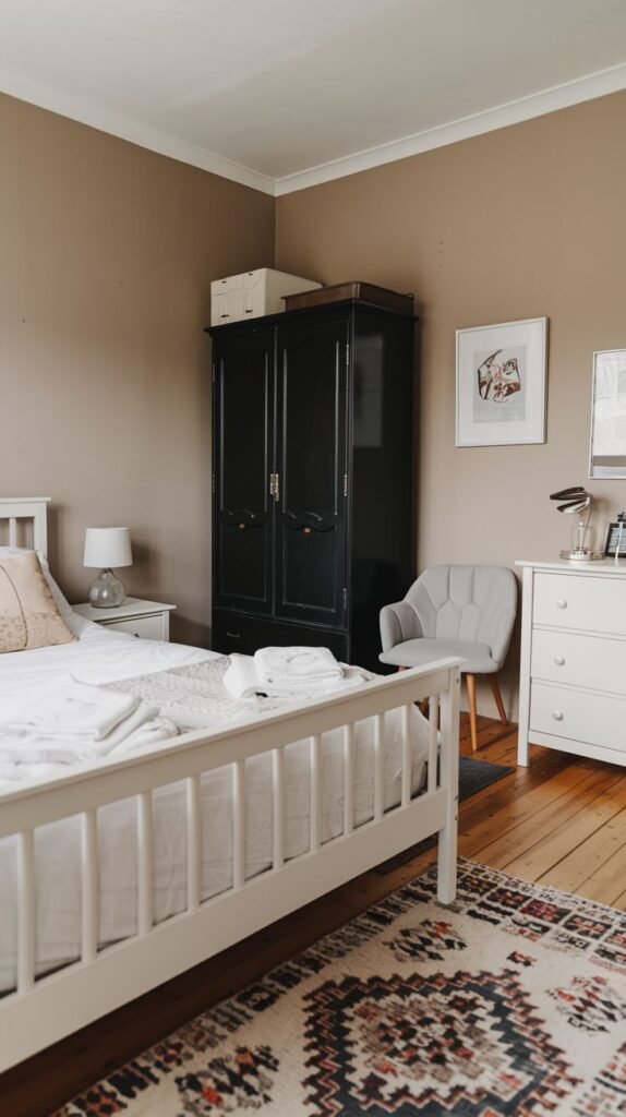 Eclectic bedroom featuring a dramatic, tall black antique armoire contrasting with a white slatted bed, white dresser, and a vibrant, patterned area rug.