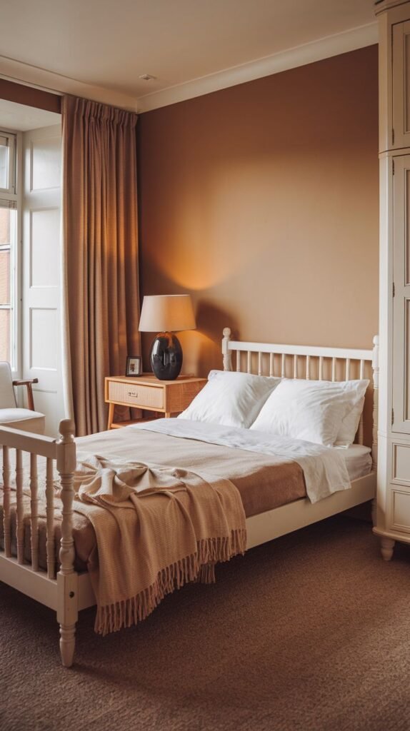 Cozy bedroom featuring a rich terracotta accent wall, a white spindle bed, a light wood nightstand, and a traditional cream-colored freestanding wardrobe.