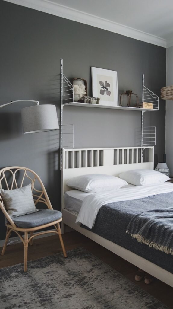 Nordic-style bedroom with dark gray walls, a white slatted bed, overhead white wire shelving, and a large wall-mounted articulated gray floor lamp positioned over the bed.