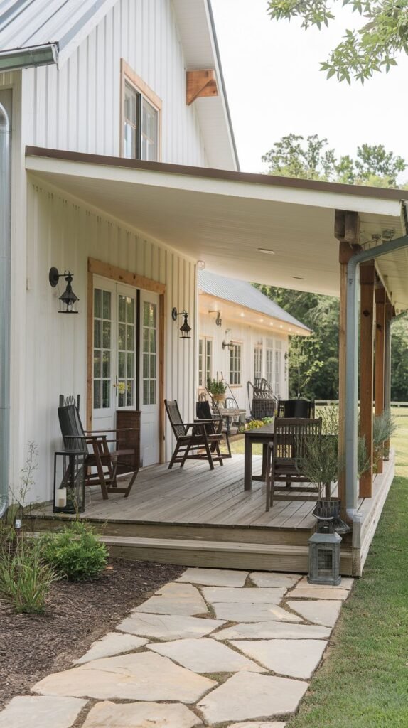 Long covered wooden deck porch with a simple shed roof and mixed seating, accessed via a wide flagstone pathway across the grass, attached to a white vertical board house.