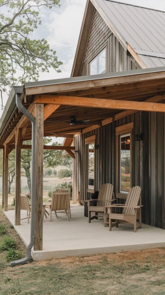 Long covered concrete patio featuring a continuous exposed wood ceiling/rafter system, running along a house clad in dark, rustic vertical siding, furnished with wooden Adirondack chairs.