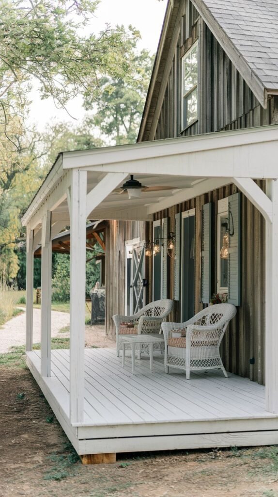 Covered white wooden deck porch with clean white structural framing, contrasting sharply with the adjacent weathered dark brown vertical wood siding of the house, furnished with white wicker chairs.