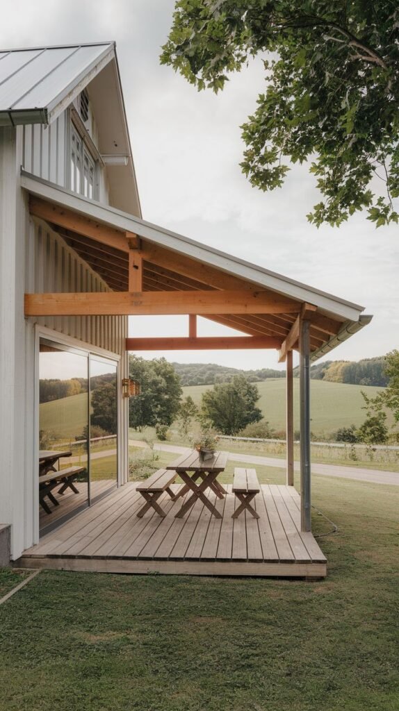 Modern farmhouse wooden deck patio with a sloped roof supported by heavy timber framing and exposed wood underside, covering a rustic wooden picnic table, adjacent to a large reflective glass door.