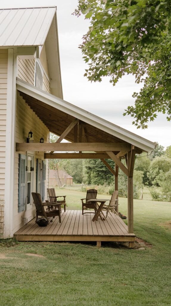 Raised wooden deck patio with a high-pitched shed roof supported by heavy exposed timber framing and bracing, furnished with wooden Adirondack chairs, attached to a light horizontal-sided house.