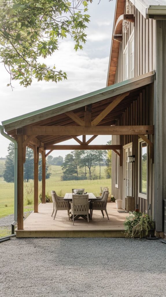 Covered raised wooden deck with a steeply pitched shed roof (with green metal visible at the edge), supported by heavy exposed timber framing, featuring woven outdoor dining furniture, attached to a rustic vertical board house.