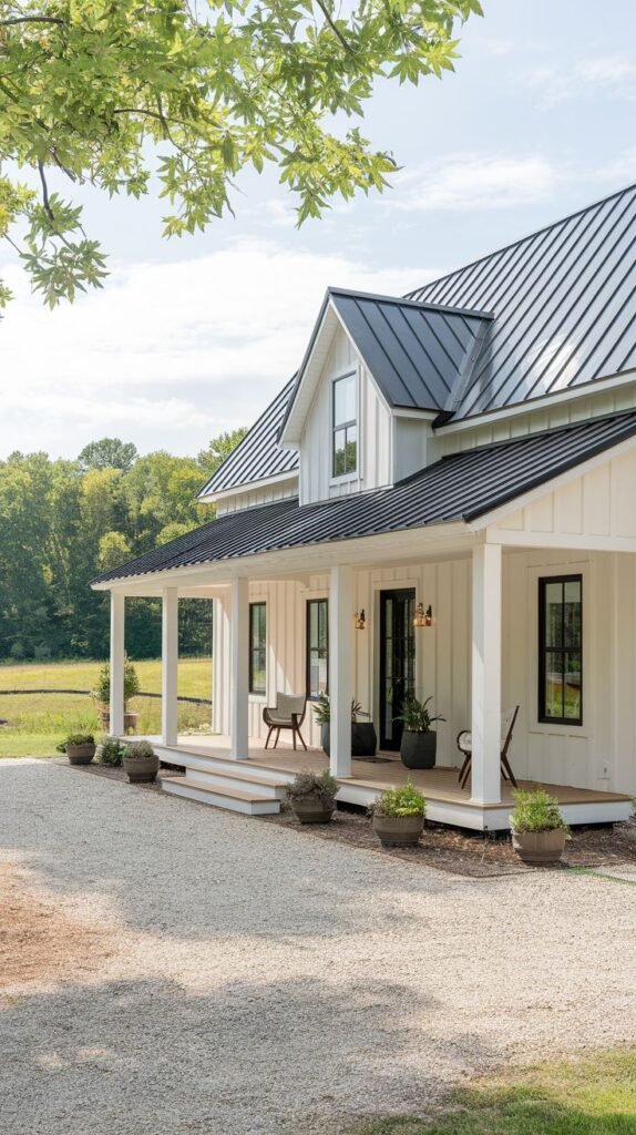 White two-story farmhouse under a black metal roof. A deep, covered porch runs the width of the house, supported by white columns, set against a large expanse of light pea gravel.