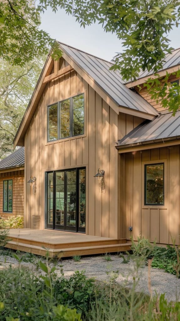 Farmhouse with mid-toned natural wood vertical siding and a dark metal roof. A high, pitched roofline covers a section leading to a simple wooden deck accessed by black-framed glass sliding doors.