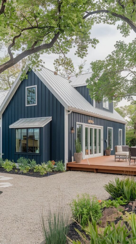 Farmhouse featuring deep navy blue vertical siding and a bright silver metal roof. A broad wooden deck extends from the side, with access provided by a series of white-framed folding glass doors.