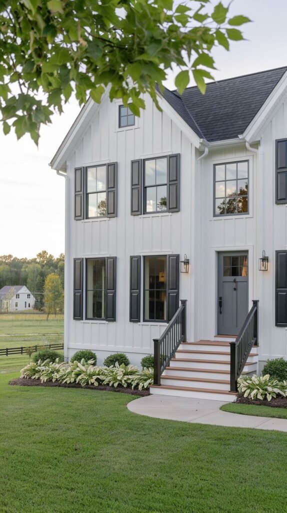Symmetrical two-story white farmhouse with a black shingled roof. The facade features black board-and-batten shutters and a gray front door, accessed by white steps with wooden treads and black vertical railings.
