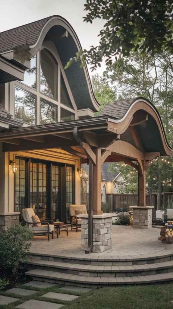 Custom architectural patio cover featuring a dramatic curved wooden roof supported by heavy timber posts resting on stacked stone bases, covering a curved patio made of light pavers.