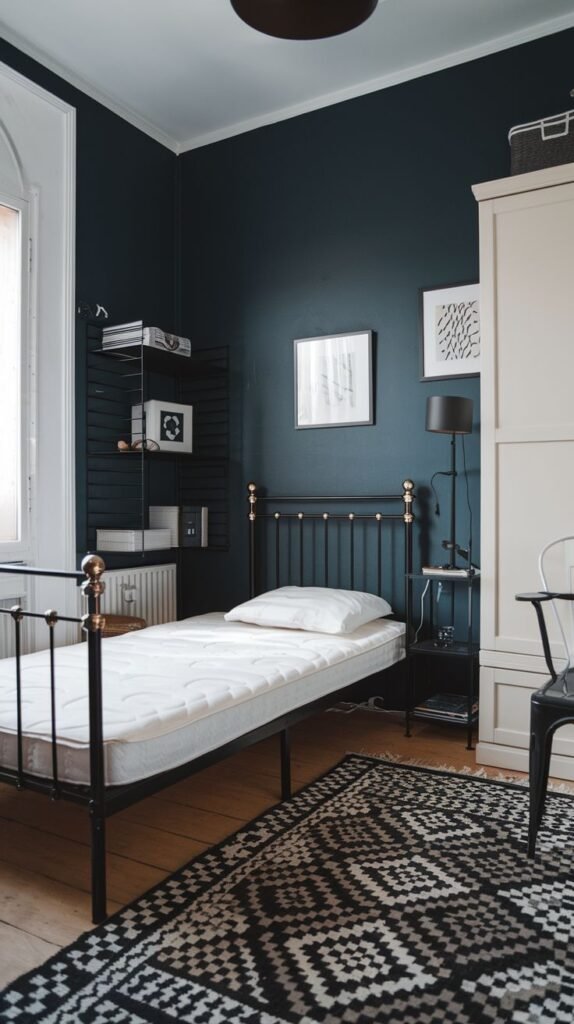 High-contrast Cozy Small Bedroom For Men with dark navy walls, a black metal bed frame detailed with brass accents, a large white wardrobe, and a black and white geometric rug.