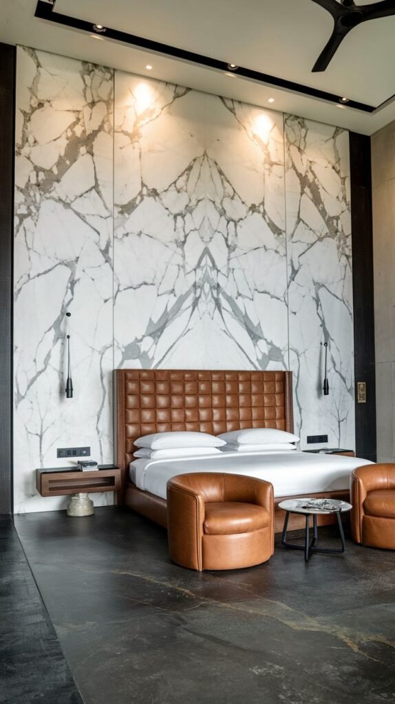 A tall, bright accent wall composed of large, book-matched white marble slabs with prominent gray veining, centered behind a brown leather headboard.