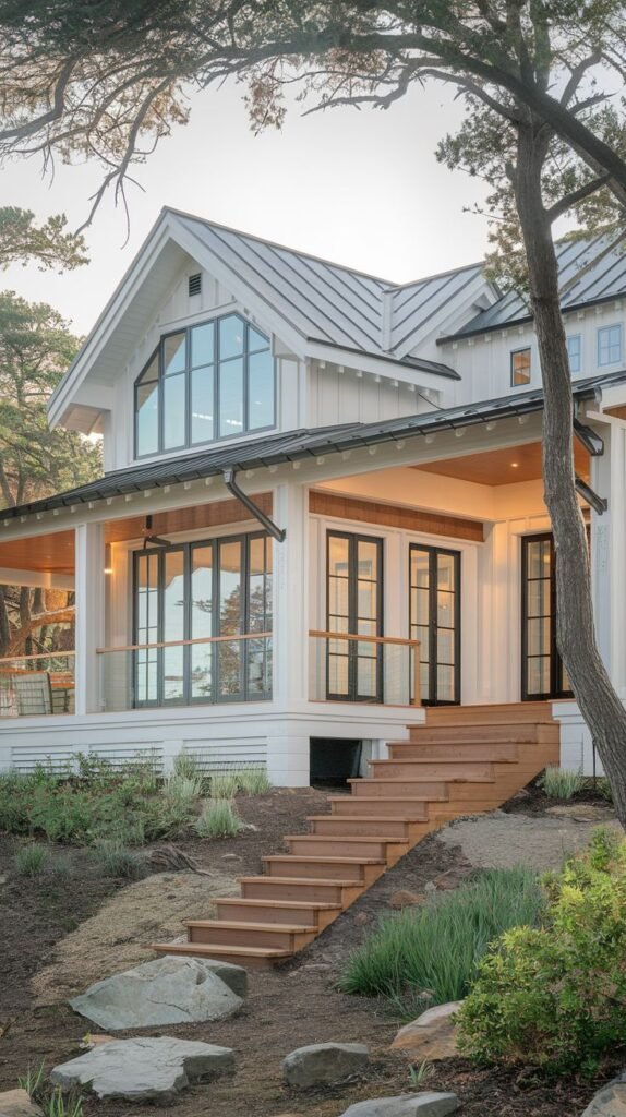 White farmhouse with a light metal roof and a deep covered porch with a natural wood ceiling. Wide wood steps lead down the sloping, naturalized landscape scattered with large stones.