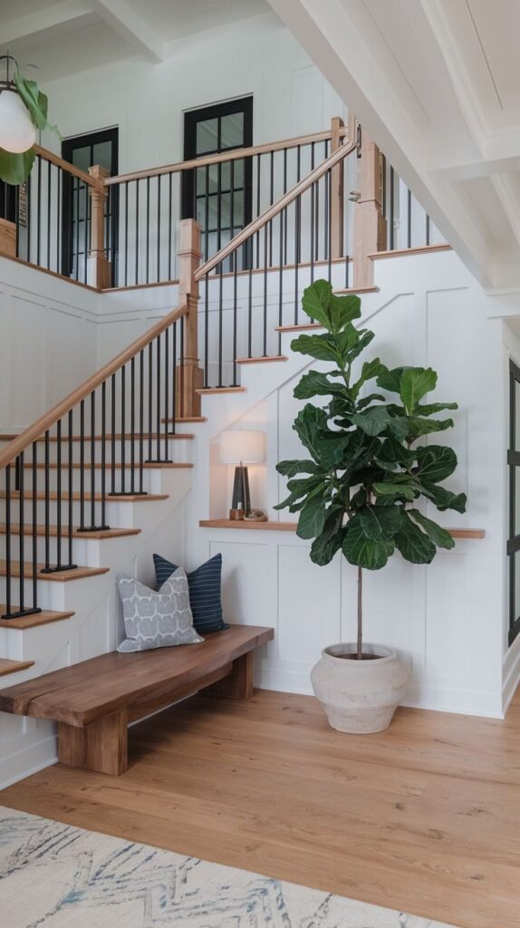 Bright modern farmhouse entryway featuring a staircase with wood treads, light wood railings, black vertical metal balusters, and a large potted fiddle leaf fig tree.