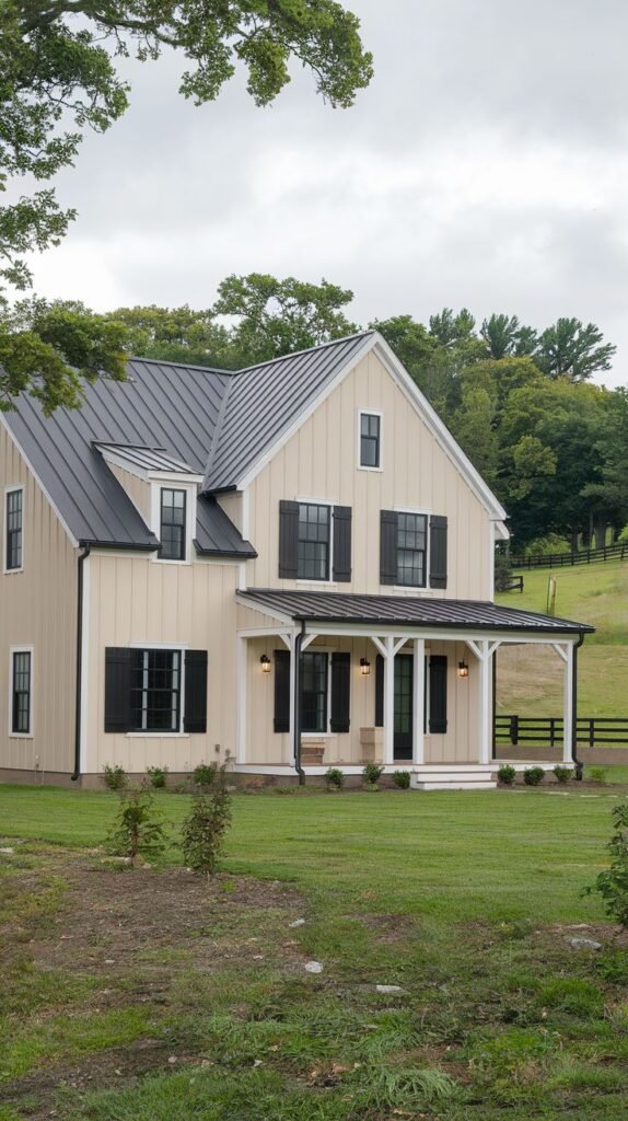 Traditional two-story farmhouse in a pale khaki color with dark black shutters, a black metal roof, and a covered front porch with white columns.