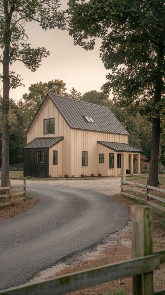 Two-story barn-style farmhouse with light tan vertical siding on the main body, a black metal roof, and a dark charcoal or black accent section on the lower level corner.