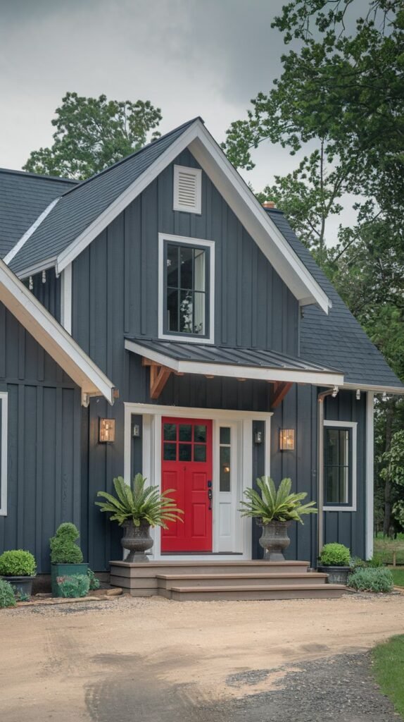 Modern farmhouse with deep charcoal board and batten siding, white trim, a dark roof, and a bright red front door framed by white sidelights, viewed from a gravel driveway.