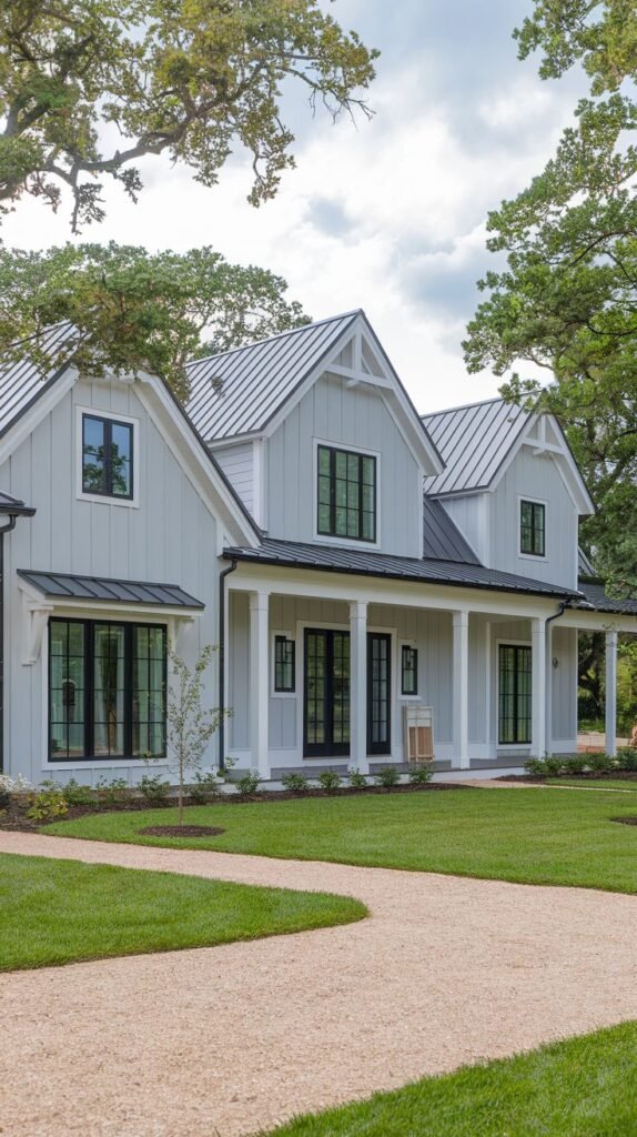 Expansive two-story farmhouse with light gray vertical siding, a white porch structure, a light gray metal roof, and multiple black-framed windows and French doors.